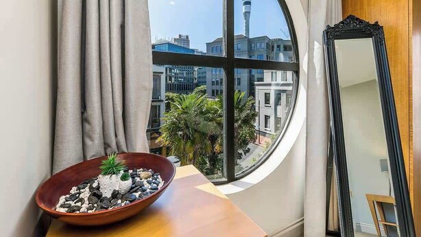 A room with a large window, a round mirror, and a wooden table with a bowl of decorative stones and a small plant. - Waterfront Beauty with Parking by Zodiak Stays (Auckland)