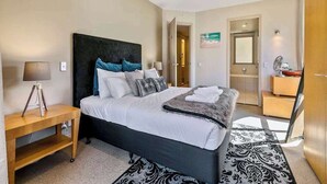 A modern hotel room with a large bed, a bedside table, a mirror, and a door leading to another room. - Waterfront Beauty with Parking by Zodiak Stays (Auckland)