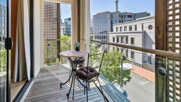 A balcony with a wooden ceiling, a table with chairs, and a view of a cityscape including a tower. - Waterfront Beauty with Parking by Zodiak Stays (Auckland)