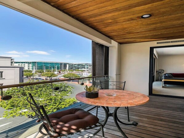 A balcony with a round table and chairs, a potted plant, and a view of buildings.