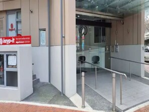 A modern building entrance with a glass door, a metal railing, and a sign for 'Keyp-it' on the left.