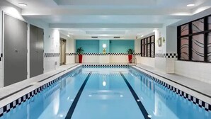 An indoor swimming pool with a checkered edge, a tiled wall with a warning sign, and a door on the left. - Cozy City Apt with Pool Gym & View by Zodiak Stays (Auckland)