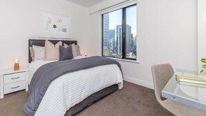 A modern bedroom with a large bed, a nightstand, a chair, and a window with a city view. - Cozy City Apt with Pool Gym & View by Zodiak Stays (Auckland)