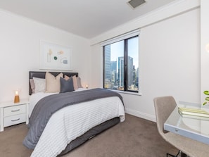 A modern bedroom with a large bed, a nightstand, a glass table, and a view of the city through a large window. - Cozy City Apt | Pool, Gym & View | Zodiak Stays (Auckland)