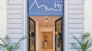 A hotel entrance with a modern design, featuring a glass door, a welcome mat, and potted plants on either side. - Tirreno Beachfront Apartments (Massa)