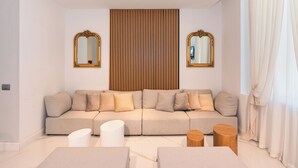 A modern living room with a beige sectional sofa, two white side tables, and a wooden accent wall with vertical slats. - Tirreno Beachfront Apartments (Massa)