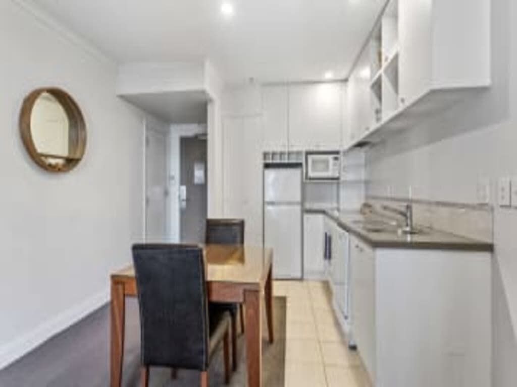 A compact kitchen with white cabinets, a microwave, and a dining area with a table and chairs.