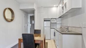 A compact kitchen with white cabinets, a microwave, and a dining area with a table and chairs. - Superking Bed in Stylish Apartment I Zodiak Stays (Auckland)