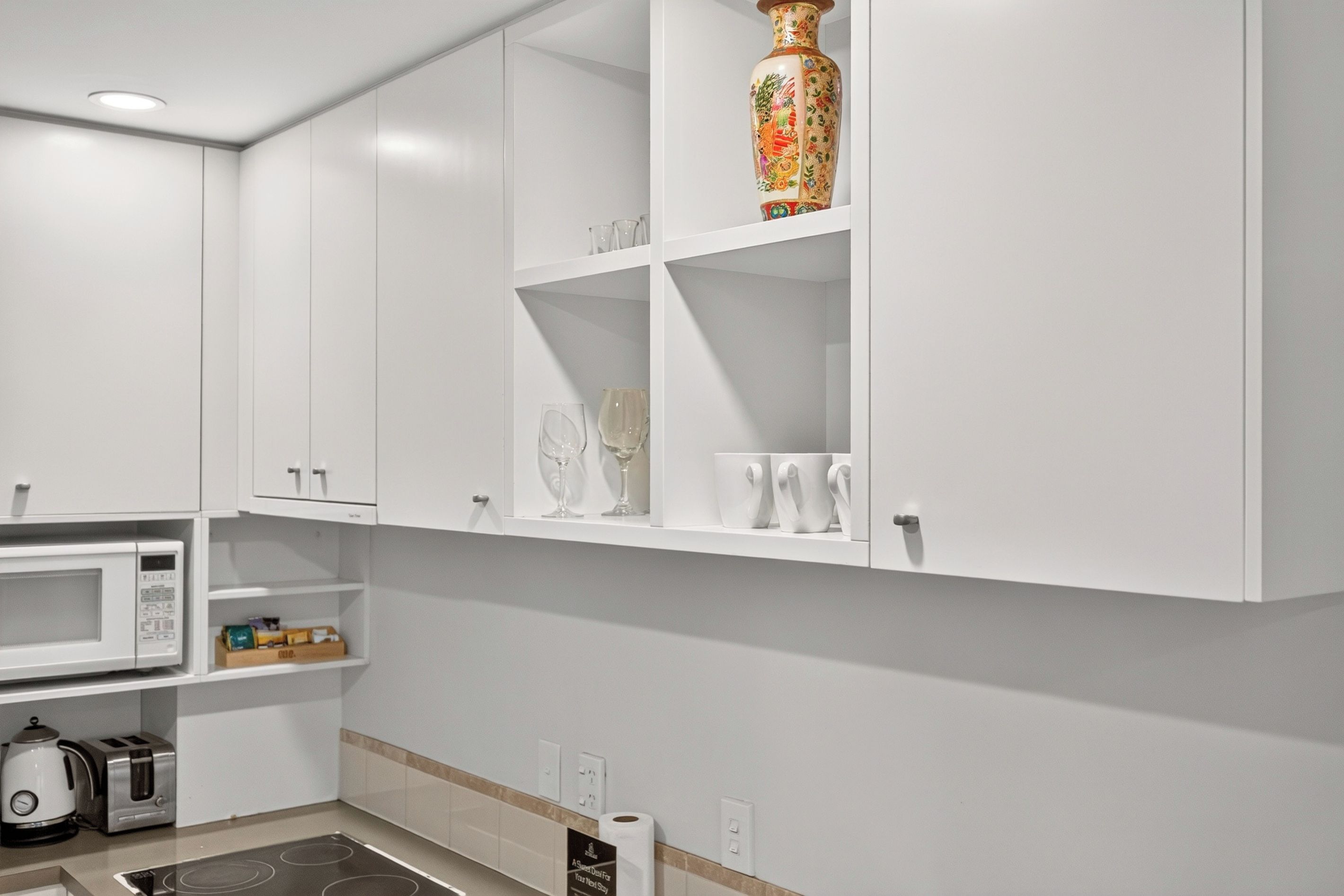 Una cocina moderna con armarios blancos, un microondas, un hervidor y una tostadora.