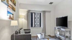 A modern living room with a sofa, a coffee table, a TV on a stand, and a window with curtains. - Superking Bed in Stylish Apartment I Zodiak Stays (Auckland)
