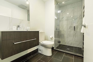 A modern bathroom with a toilet, vanity, and a glass shower enclosure.