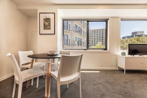 A modern hotel room with a dining area, a TV, and a window with a city view. - Park Views in CBD Next to Myers Park by Zodiak (Auckland)