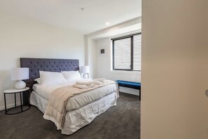 A bedroom with a bed, bedside lamps, a bench, and a window with blinds. - Park Views in CBD Next to Myers Park by Zodiak (Auckland)