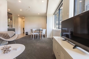 A modern living room with a flat-screen TV, a dining table with chairs, a sofa, and a carpeted floor. - Park Views in CBD Next to Myers Park by Zodiak (Auckland)