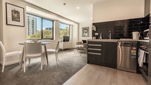 A modern kitchen with a built-in dishwasher, a dining area with a table and chairs, and large windows offering a view of the cityscape. - Beautiful 2BR Unit next to Myers Park Zodiak Stays (Auckland)