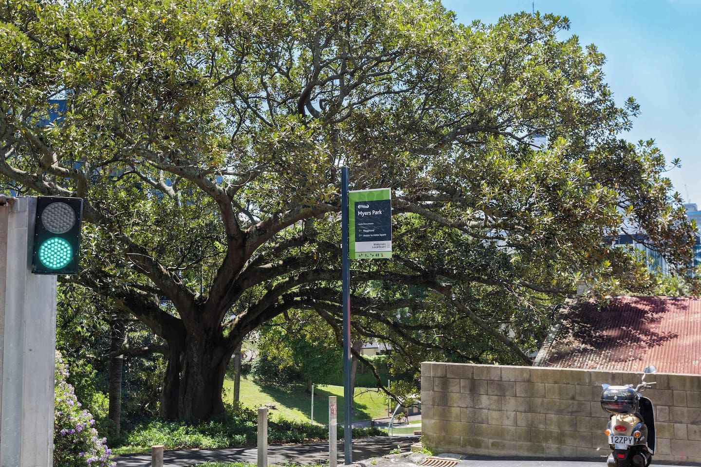 Un semáforo, un cartel indicando Myers Park y una scooter estacionada junto a una pared.