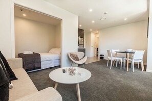 A modern hotel room with a bed, a sofa, a dining table with chairs, and a small round table with a decorative item. - Park Views in CBD Next to Myers Park by Zodiak (Auckland)