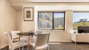 A modern hotel room with a dining area, a television, and a window with a city view. - Beautiful 2BR Unit next to Myers Park Zodiak Stays (Auckland)