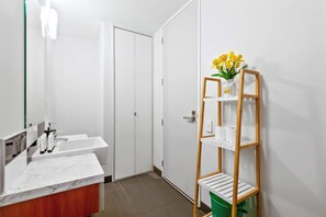A modern bathroom with a marble sink, a wooden shelf with toiletries, and a green trash bin.