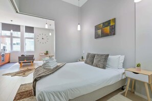 Ein modernes Schlafzimmer mit einem großen Bett, einer Uhr, einem Gemälde und Blick auf die Küche.