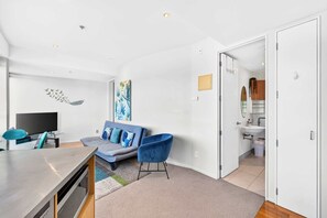 Ein modernes Wohnzimmer mit Flachbildfernseher, einer blauen Couch mit Kissen, einem blauen Sessel und einem Gemälde an der Wand.