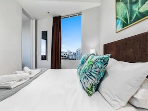 Une chambre d’hôtel avec un lit, une fenêtre donnant sur un paysage agréable, une porte et un tableau accroché au mur.