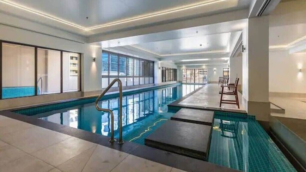 Ein moderner, überdachter Pool mit klarem Wasser, gefliestem Boden und einer Sitzgelegenheit mit Stühlen.