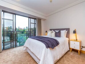 A bedroom with a large bed, a nightstand, and a view through a sliding glass door.