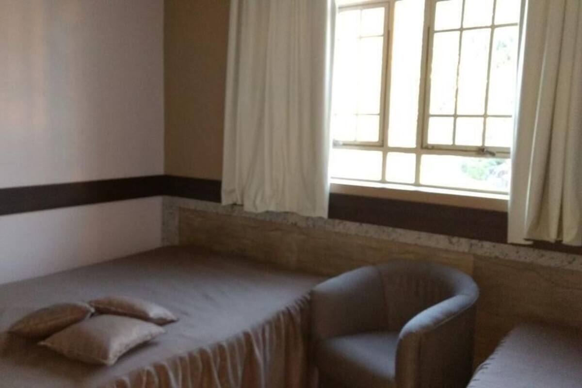 Une chambre avec un lit simple, une chaise et une fenêtre avec des rideaux.