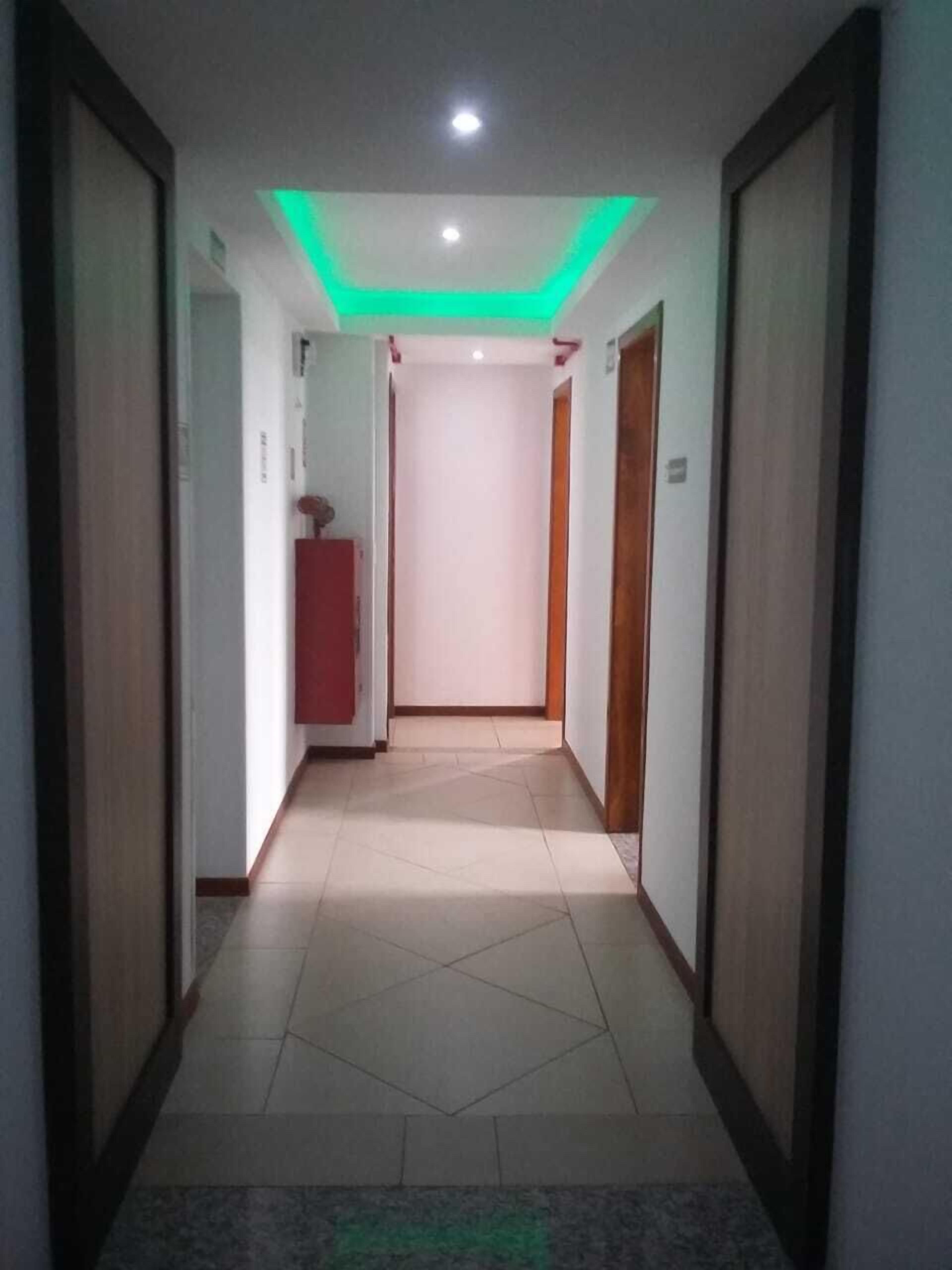 Un pasillo con suelo de baldosas, una lámpara empotrada en el techo y una puerta al final.