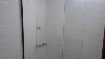 Un espacio de ducha pequeño y cerrado con puerta de vidrio, un inodoro y un escalón que lleva a la ducha.