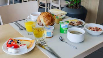 A breakfast table with a croissant, orange juice, yogurt, and cereal.
