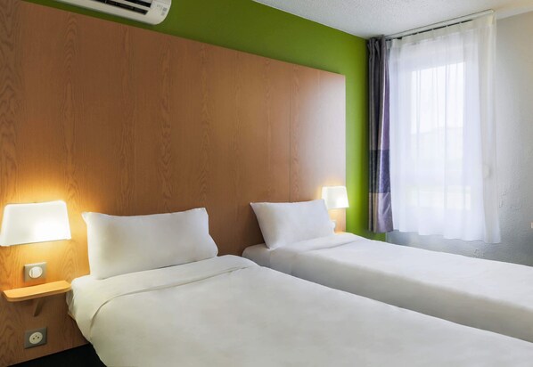 Habitación de hotel con dos camas, cabecero de madera, lámparas de noche y una ventana con cortinas traslúcidas.