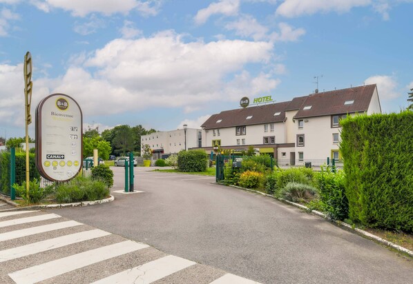 A hotel entrance with a signboard, a gated driveway, and a building with multiple windows.