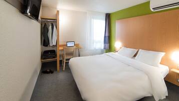 Una camera d'hotel con un letto, una scrivania con un portatile, una TV a parete e un appendiabiti.