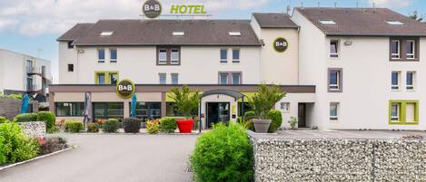 A B&B hotel with a modern design, featuring a central entrance, outdoor seating area, and a stone wall.