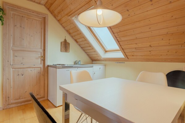 A room with a sloped ceiling, a skylight, a white table, and a compact kitchenette. - Lovely House in Tórshavn (Hoyvík)