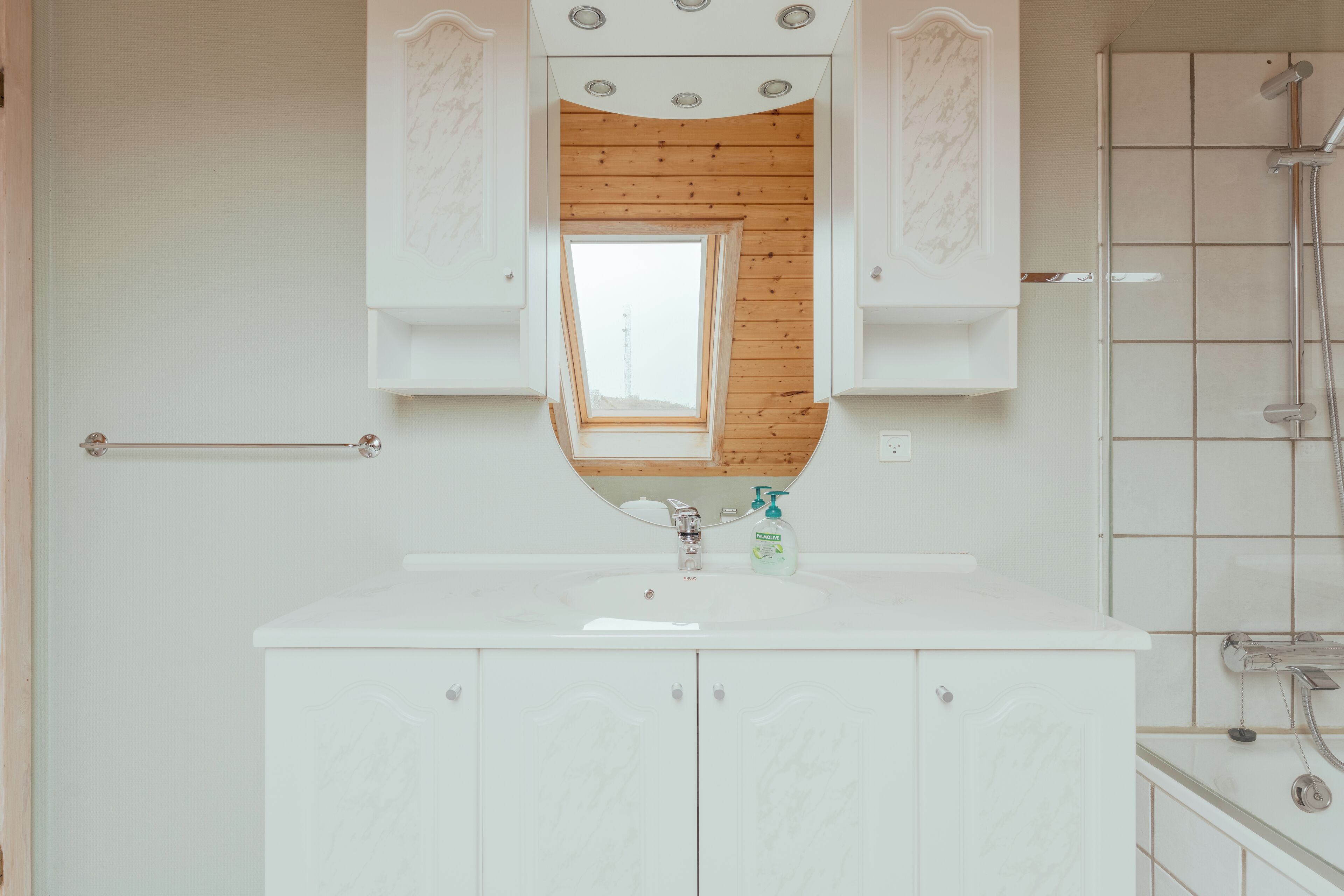 A bathroom with a white vanity, a mirror, a wooden ceiling, and a shower area.