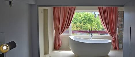 Une salle de bain moderne avec une baignoire sur pieds, une fenêtre avec des rideaux et une vue dégagée sur l’extérieur.