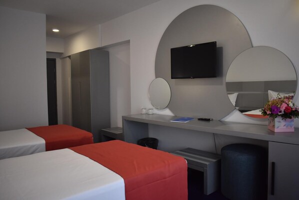 A hotel room with two beds, a desk with a flat-screen TV, a mirror, and a small table with a vase of flowers. - Hotel Europolis (Tulcea)
