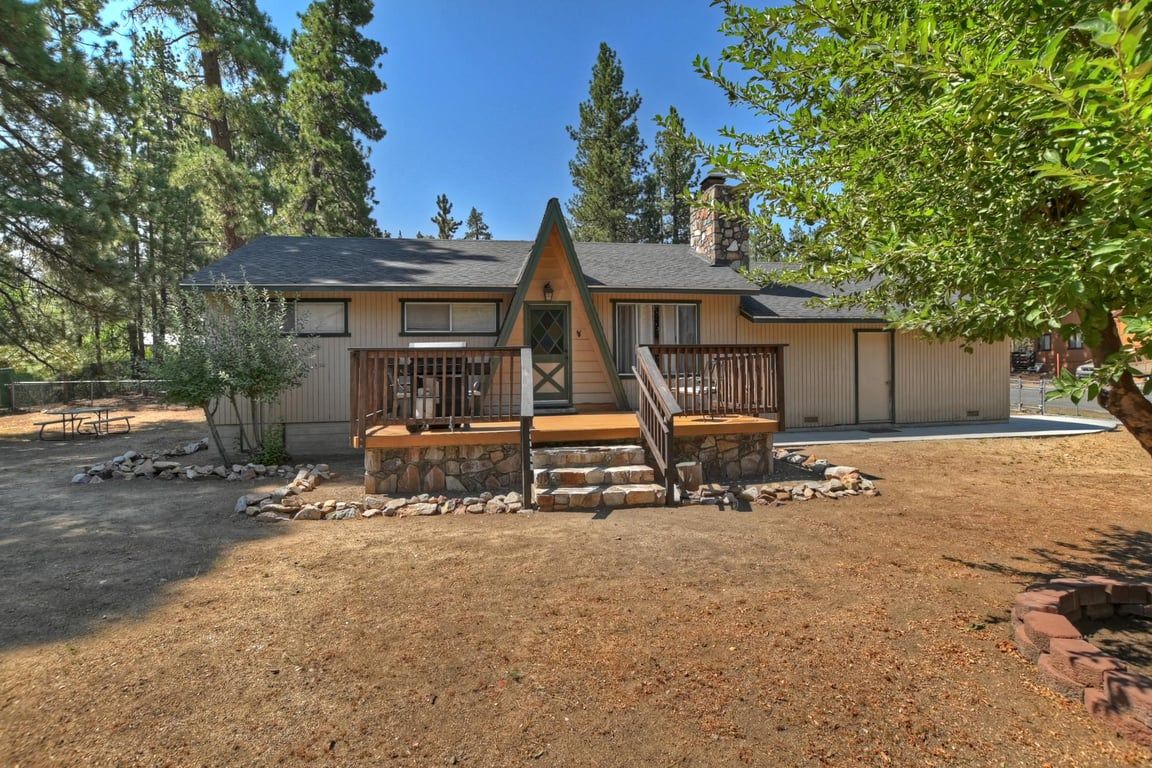 A cabin with a stone foundation, wooden deck, and a small porch.