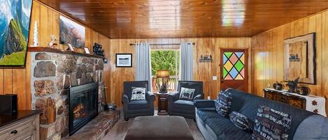 A cabin interior with a stone fireplace, wooden walls, a sofa, and a television.