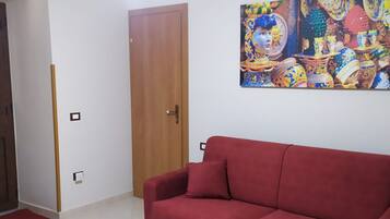 Une pièce avec un canapé rouge, une porte en bois et un tableau coloré accroché au mur.