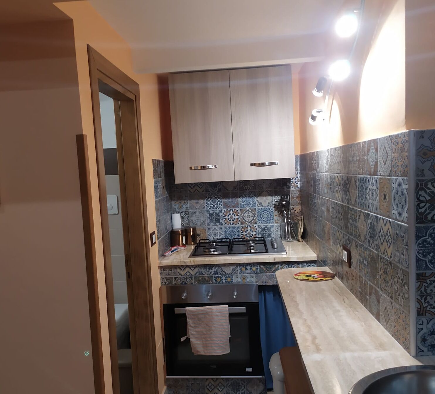 Cozinha compacta com armários de madeira, fogão a gás e azulejos estampados.