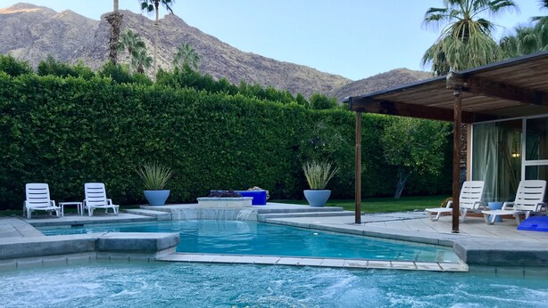 A swimming pool with lounge chairs and a waterfall feature, surrounded by greenery and a mountain backdrop. - Rose Vista Las Palmas Special Summer Rates Now In Effect (Palm Springs)