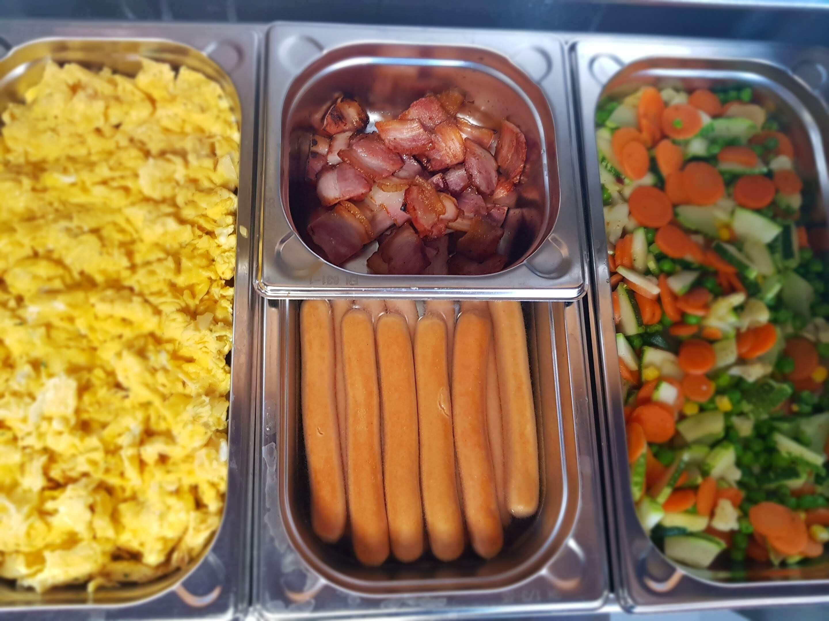 Un bufé con huevos revueltos, tocino, salchichas y una ensalada de verduras.