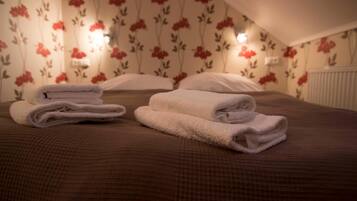 A hotel room with floral wallpaper, a bed with a brown bedspread, and two neatly folded towels on the bed.