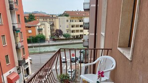 Un balcon donnant sur une rivière et des immeubles, des chaises en plastique blanches, une plante en pot et un panneau de signalisation « stop » sur la rue.