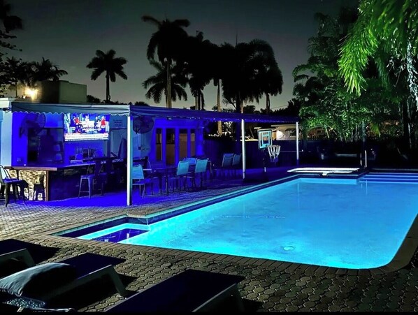 Swimming pool at night with surrounding palm trees and a hot tub area . 