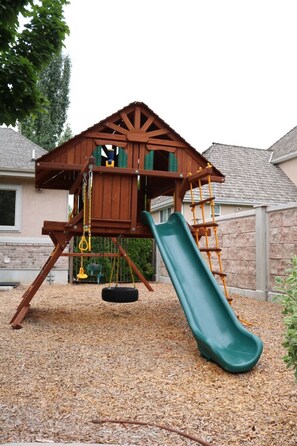 Children can play on the wooden play structure with a slide and rope ladder.